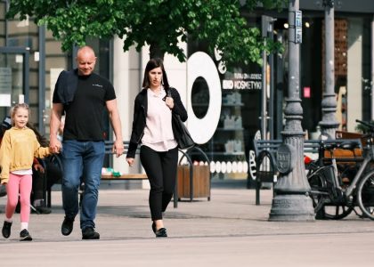 A family walks past storefronts and bicycles in a lively shopping district.